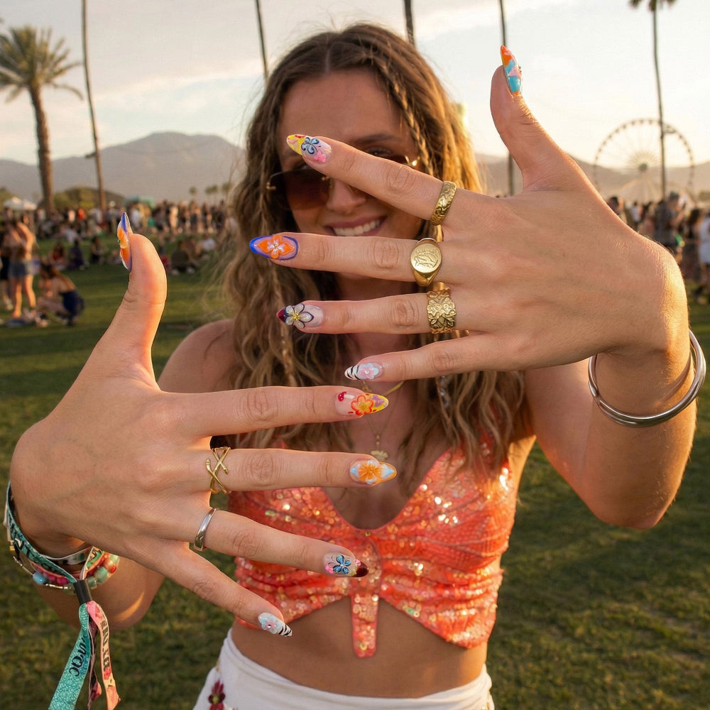 A vibrant soul unleashes her floral fantasy while adorned in sparkling brilliance and statement rings. Ten explosive nail canvases bursting with fearless florals, electrifying patterns, and show-stopping embellishments — your fingertips reborn as unapologetic masterpieces of self-expression. Blue and orange nails.