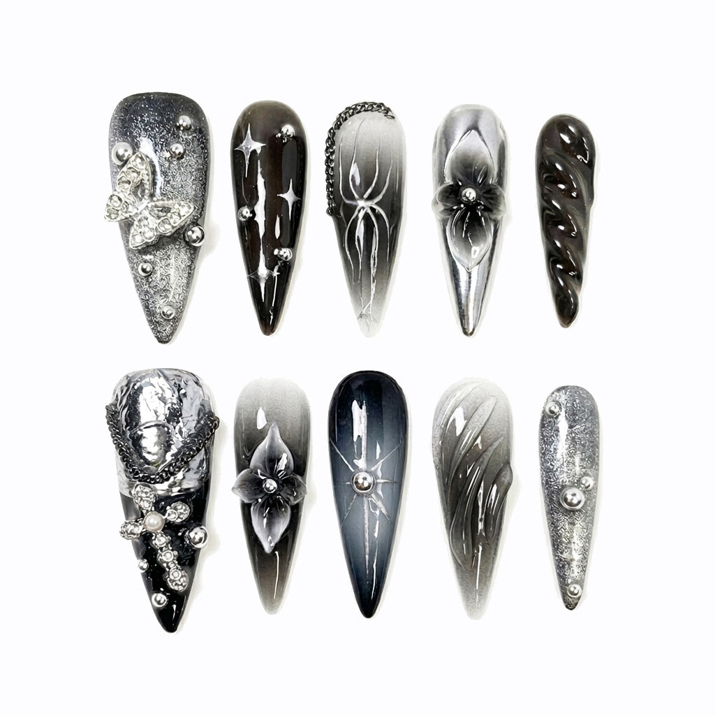 Ten stylish stiletto nails in black, gray, and silver shades with various decorations like flowers, chains, and sparkles.