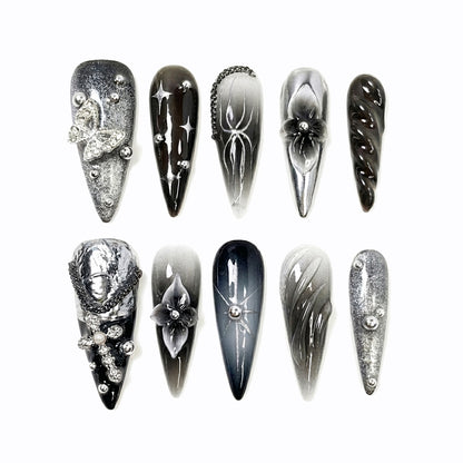Ten stylish stiletto nails in black, gray, and silver shades with various decorations like flowers, chains, and sparkles.