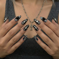 Ten black almond press-on nails with silver and rhinestone designs, including hearts and skulls.