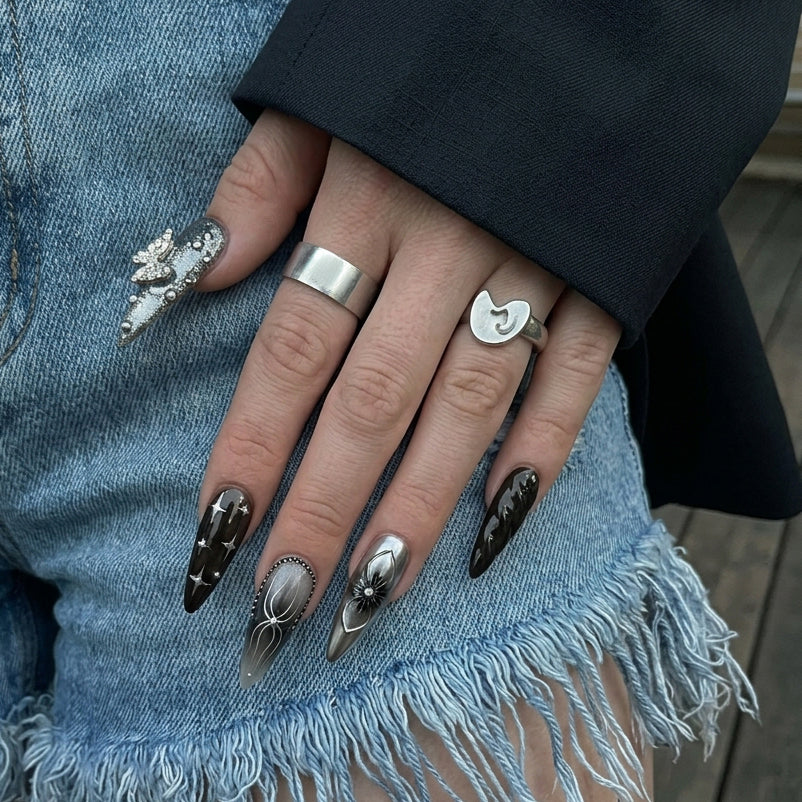 Ten stylish stiletto nails in black, gray, and silver shades with various decorations like flowers, chains, and sparkles.