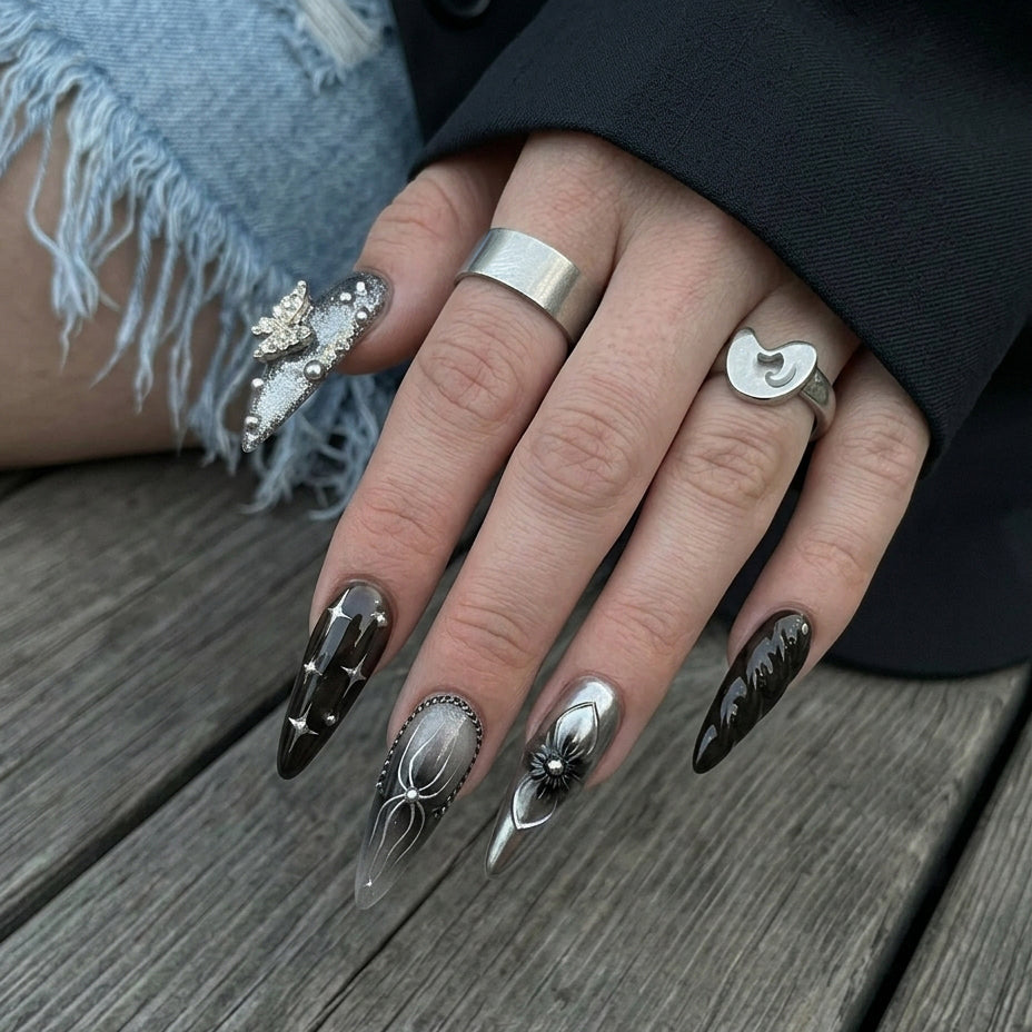 Ten stylish stiletto nails in black, gray, and silver shades with various decorations like flowers, chains, and sparkles.