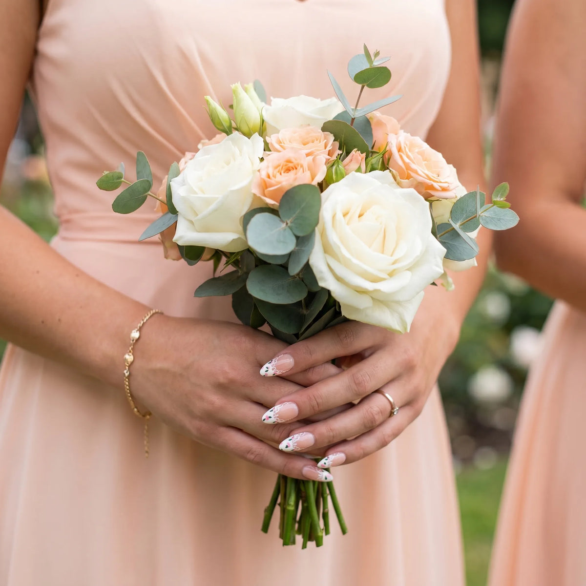 Ivory Bloom French nail art with white lace scallop French tips and pink rose bud floral details on almond nails, bridesmaid holding peach and white rose eucalyptus bouquet