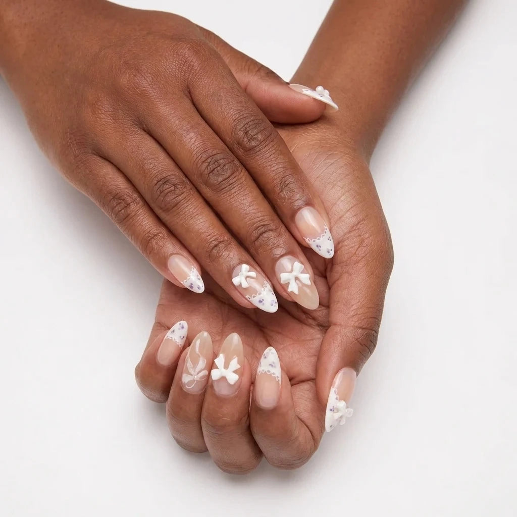 Ribbon Muse sheer nail art with 3D white ribbon bow, scallop lace French tips and purple floral accents on almond nails, close up showing swirl detail on white background