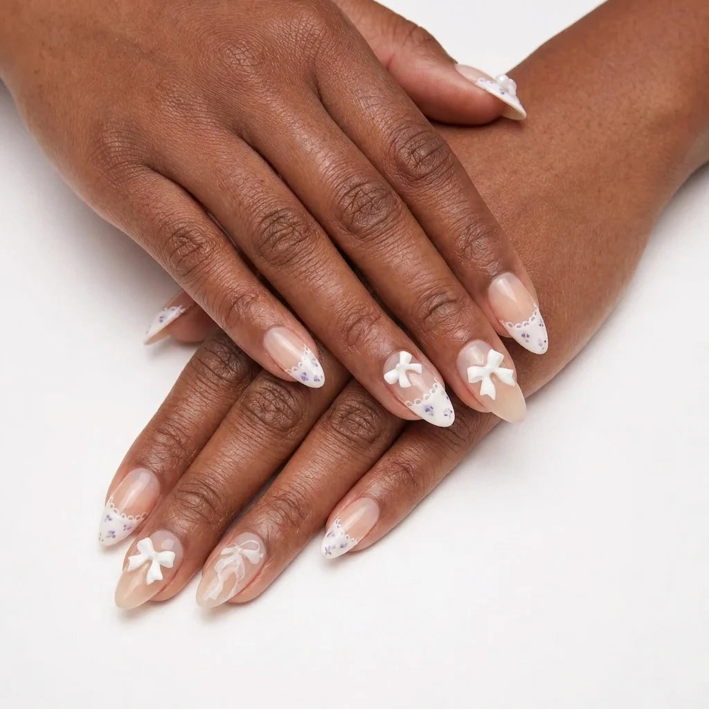 Ribbon Muse sheer nude nail art with 3D white bow charms, lace scalloped French tips and tiny lavender floral patterns on almond nails against white background