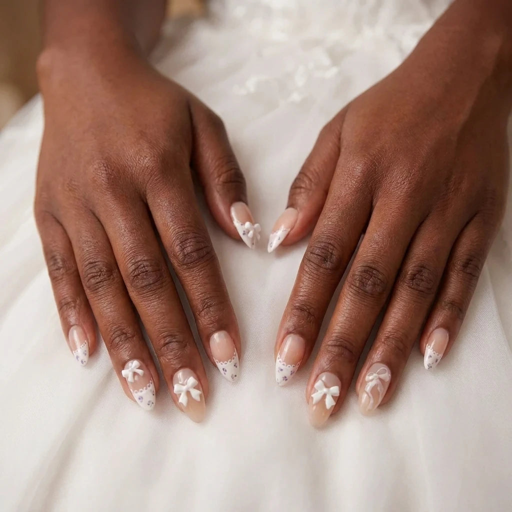 Ribbon Muse elegant bridal nail art with 3D white bow accents, white scalloped lace tips and delicate purple floral details on almond nails, both hands on white fabric