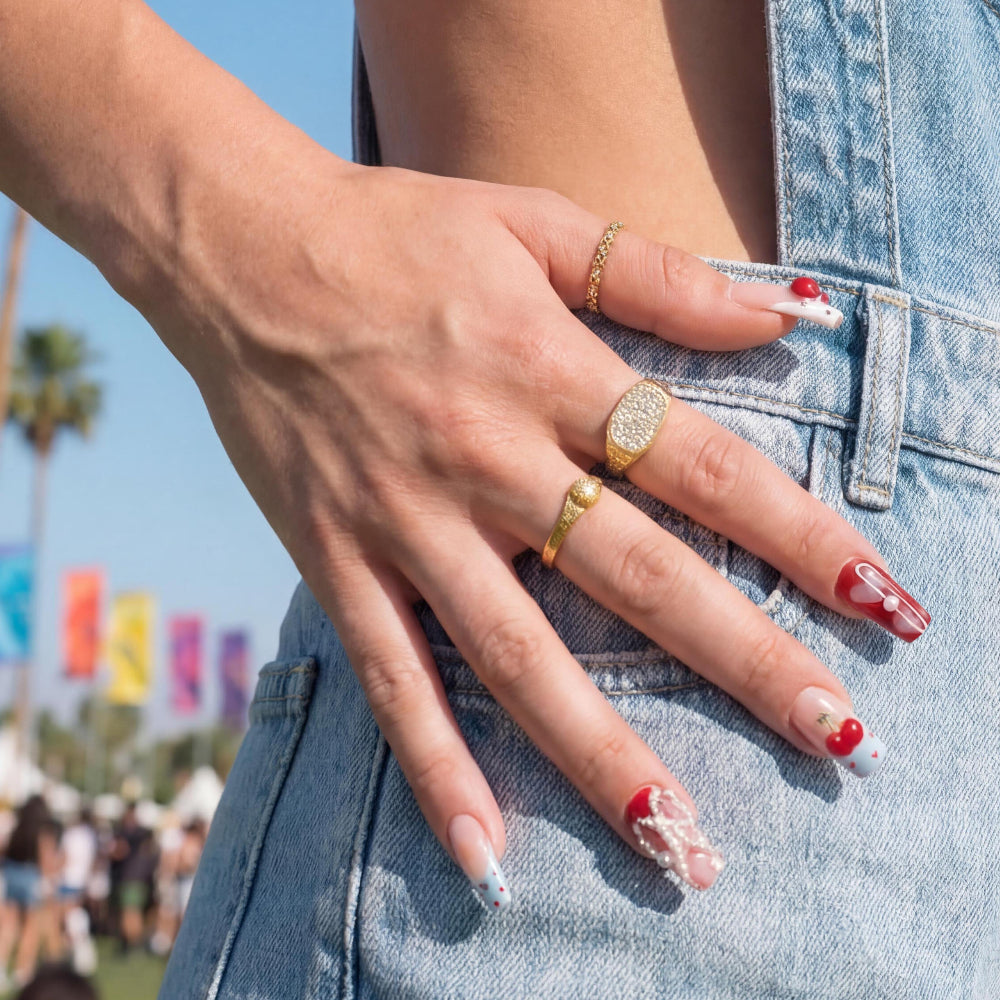 Nail art with a cherry theme featuring red, blue, and white designs with pearls