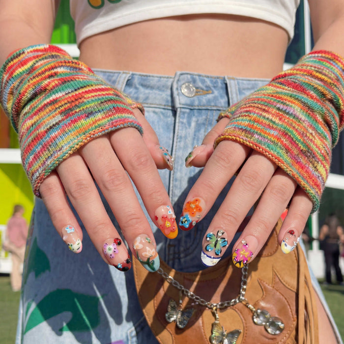 Colorful nail art set with flowers, butterflies, ladybug and gems on nude nails. Close-up of hands with colorful nail art wearing a rainbow fingerless glove