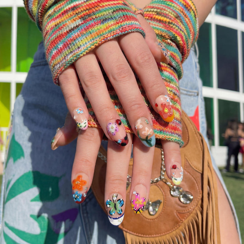 Colorful nail art set with flowers, butterflies, ladybug and gems on nude nails. Close-up of hands with colorful nail art wearing a rainbow fingerless glove,.