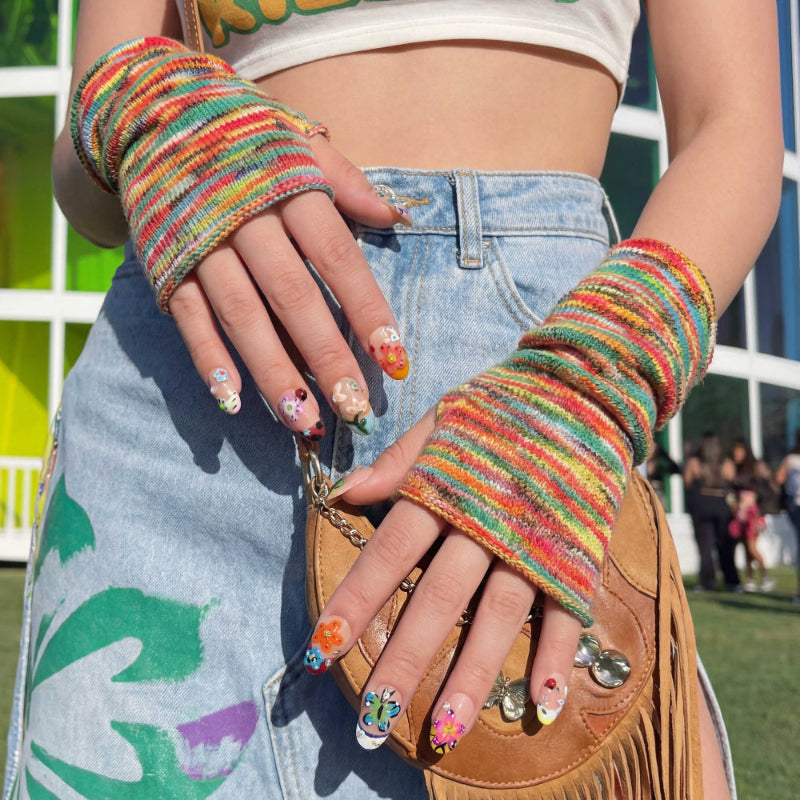 Colorful nail art set with flowers, butterflies, ladybug and gems on nude nails. Close-up of hands with colorful nail art wearing a rainbow fingerless glove